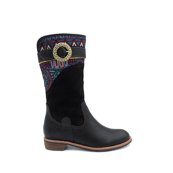 A black velvet knee-high boot with a decorative pattern and a circular embellishment on the ankle.