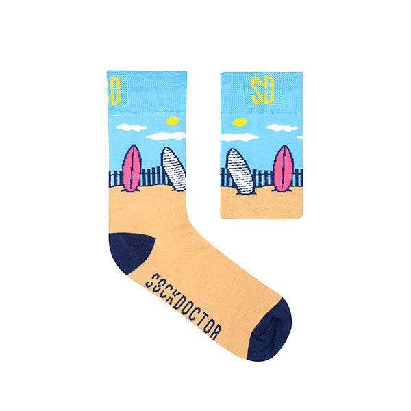 A pair of socks with a beach and surfboard design, predominantly blue and beige in color, with the brand name 'SOX DOCTOR' on the ankle area.