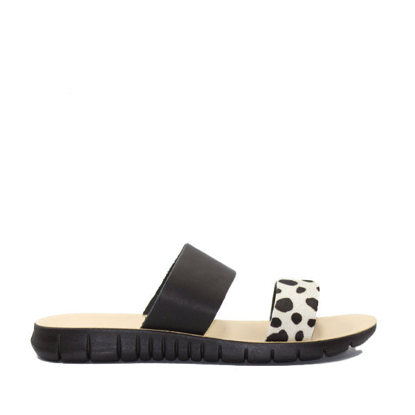 A black and white slide sandal with a Dalmatian print on one strap, other strap plain black.
